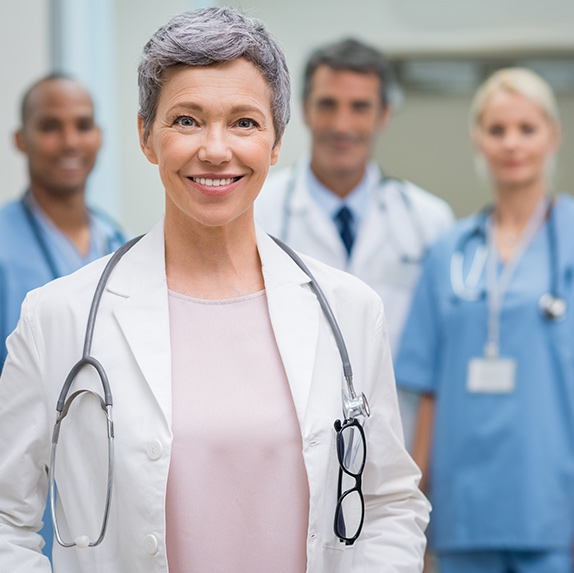 Happy female doctor smiling with her stethoscope around her neck with 3 fellow doctors standing behind her in the background
